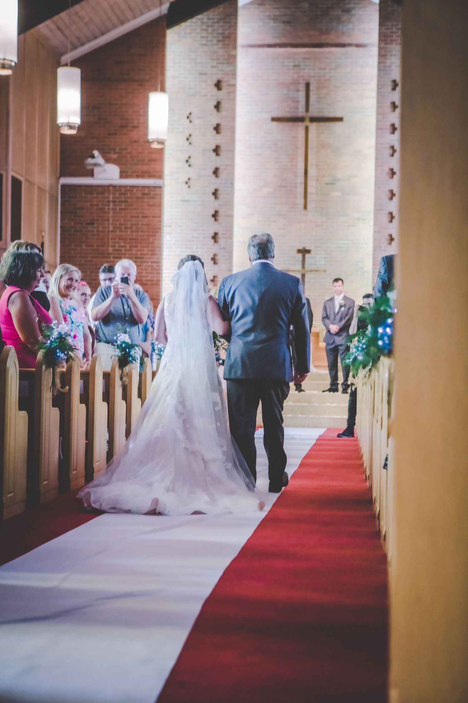 Inside a brick church with traditional cross and altar, wedding guests look on during the ceremony.