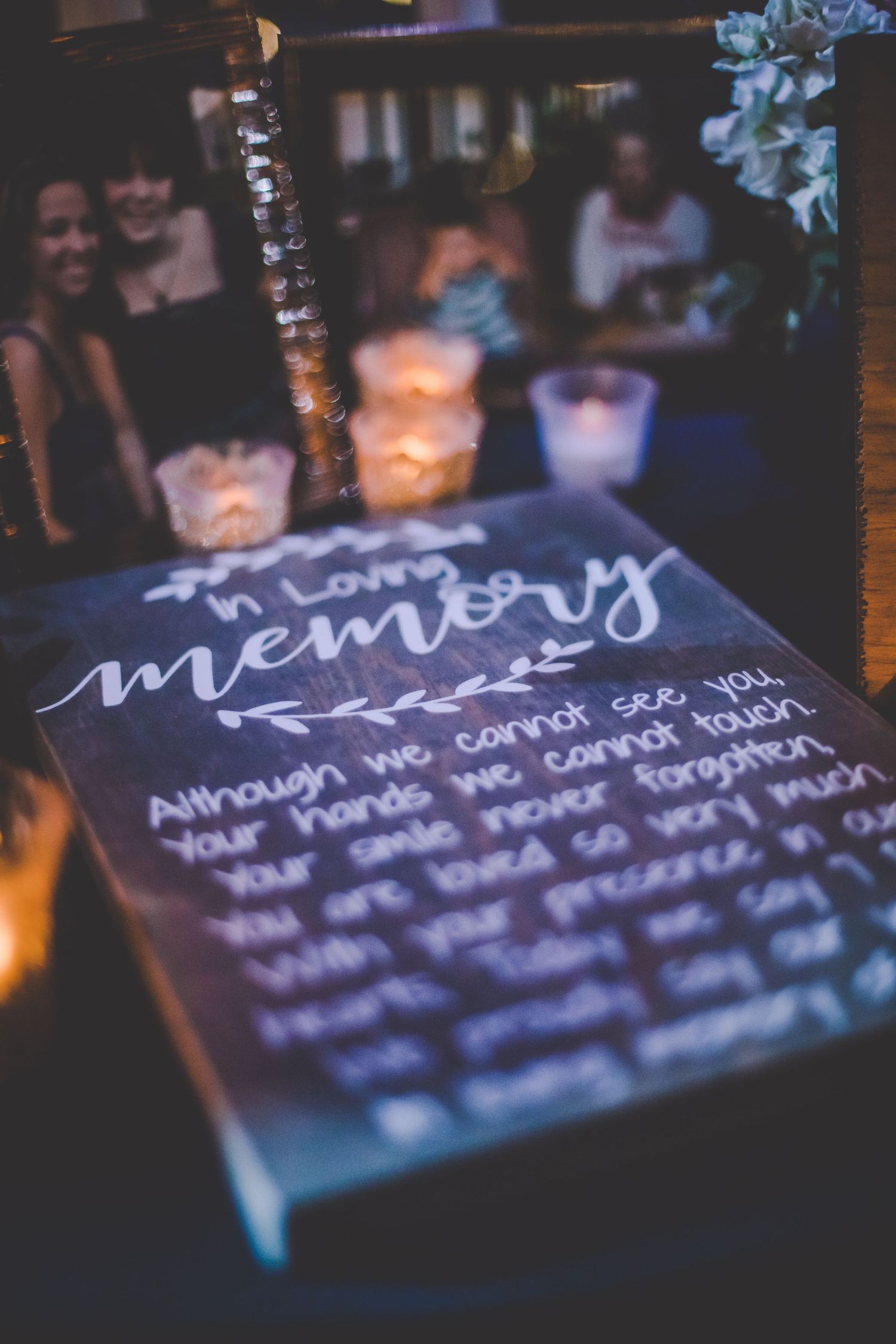 A candlelit memorial sign with handwritten text and bokeh lights in the background.