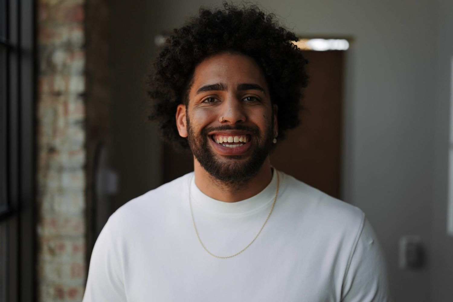 A person in a white shirt smiles warmly against a blurred brick wall background.
