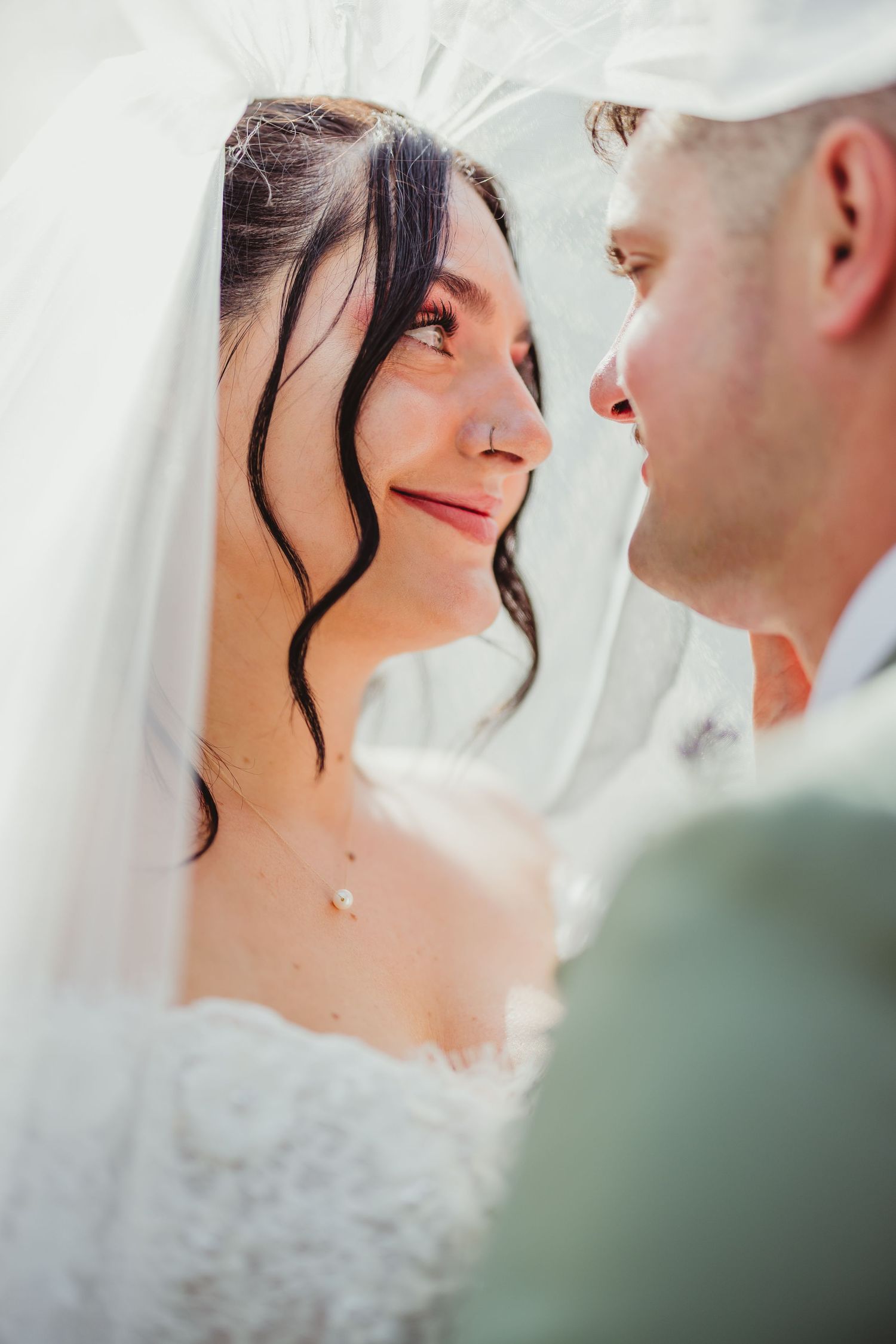 Bride and groom share an intimate gaze under a white veil on their wedding day.