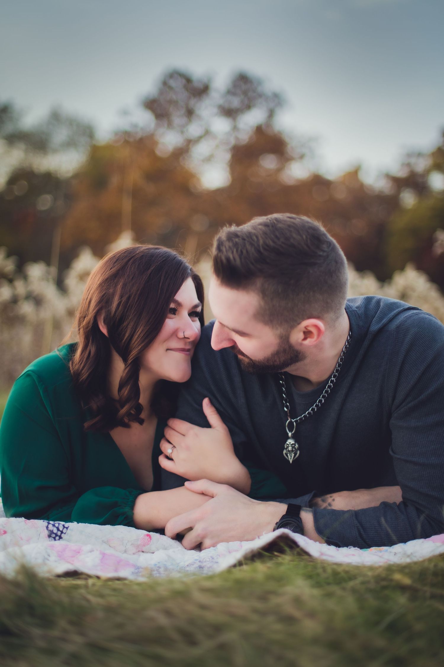 Couple sharing tender moment while lying on blanket in field during fall season.