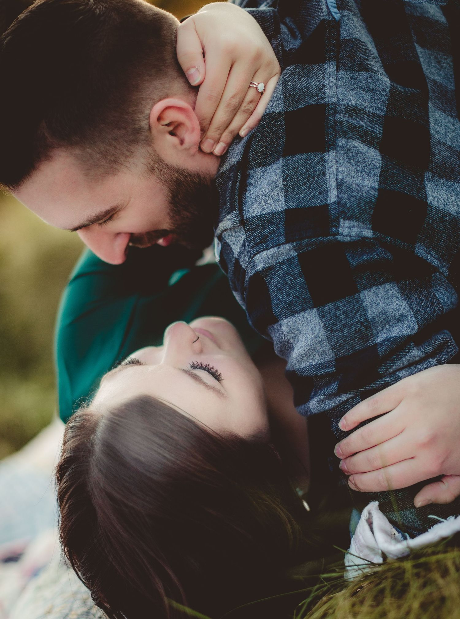 Close-up portrait of a couple sharing a tender moment while lying on grass.