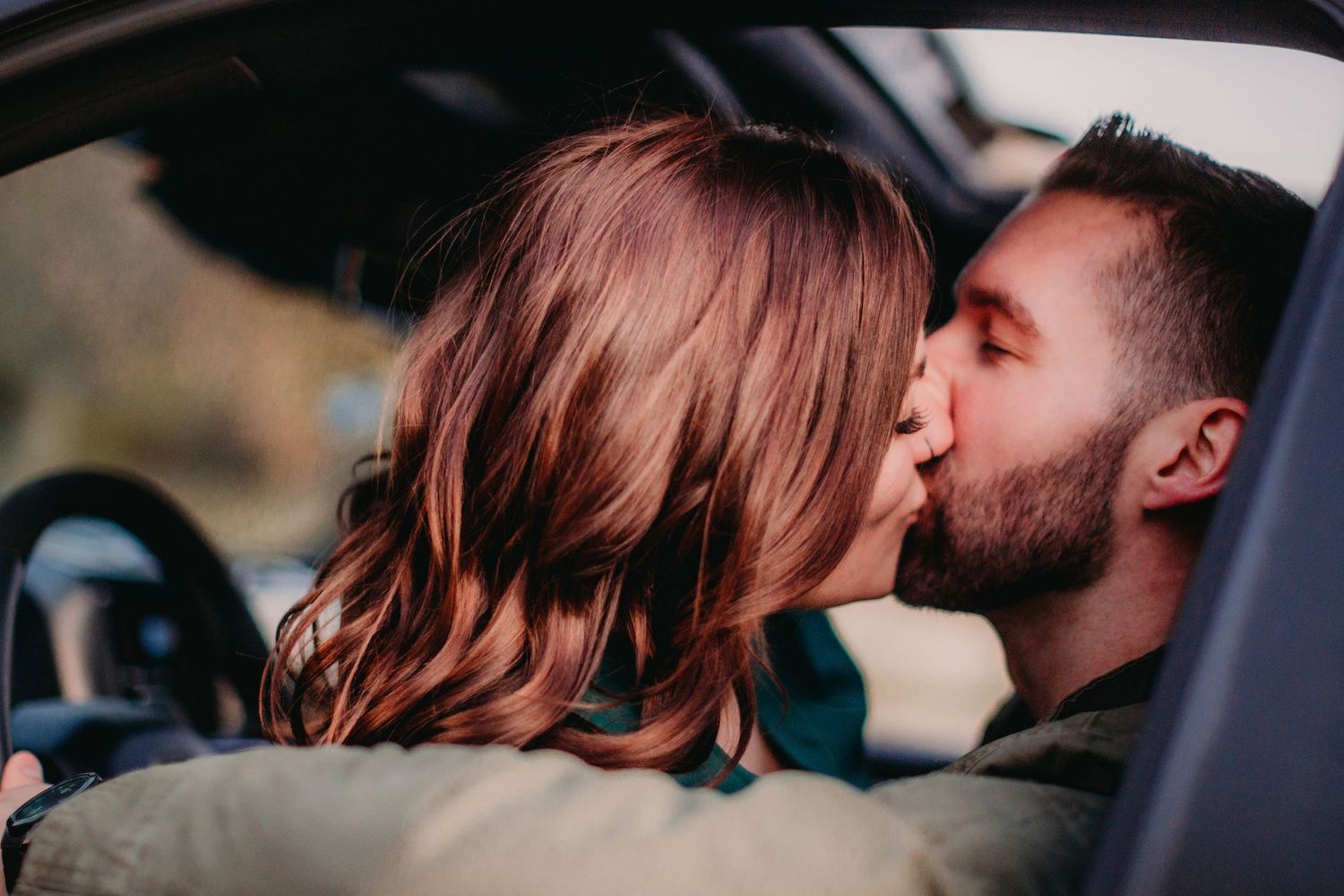Intimate kiss captured through car window in natural lighting.