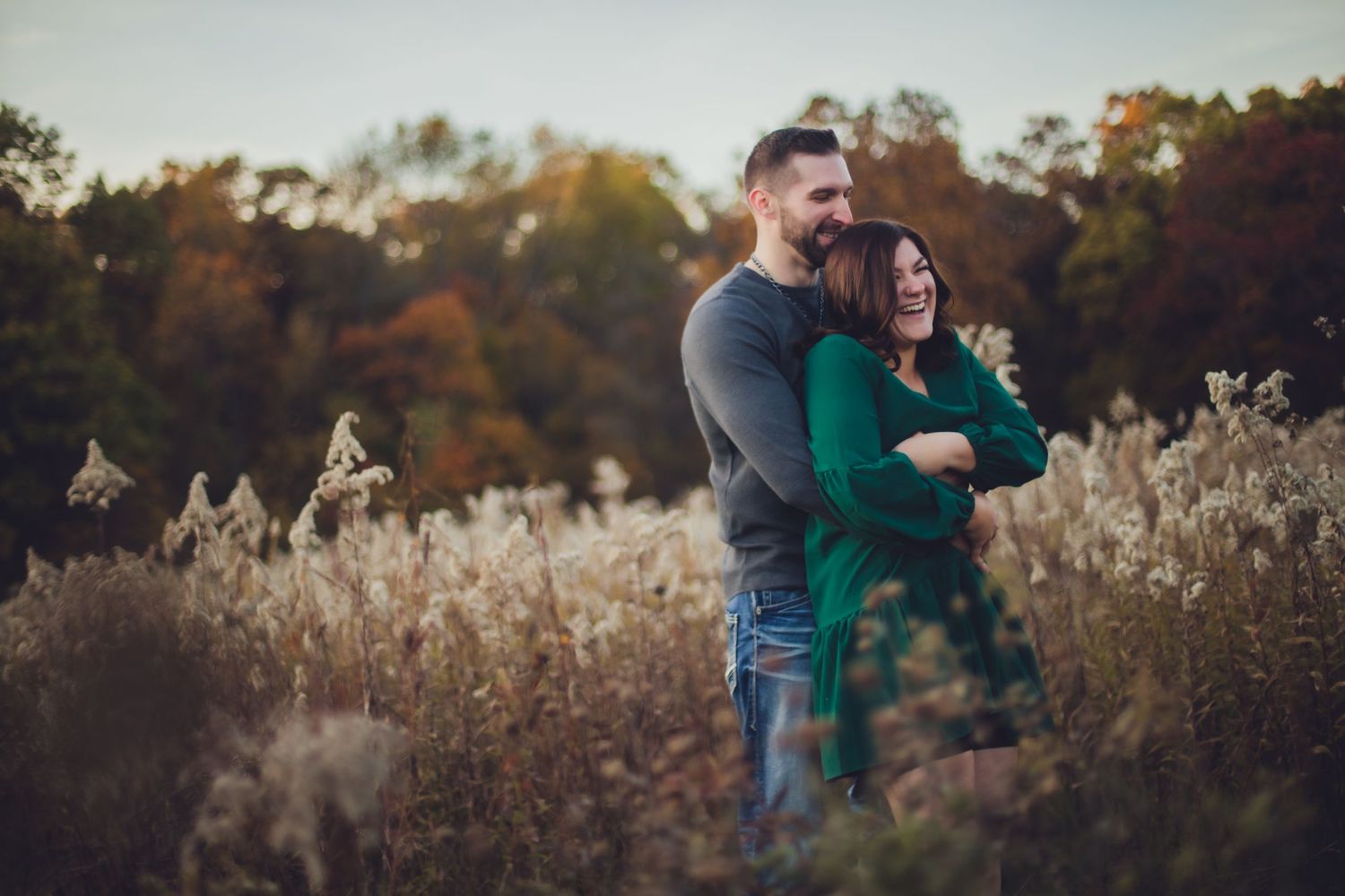 Intimate outdoor engagement photos captured in a rustic field during golden hour.