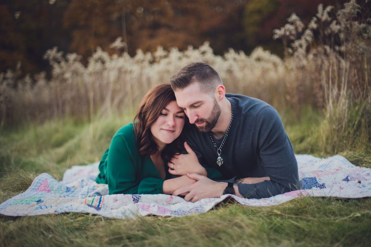 Couple snuggling close together on picnic blanket surrounded by fall foliage.