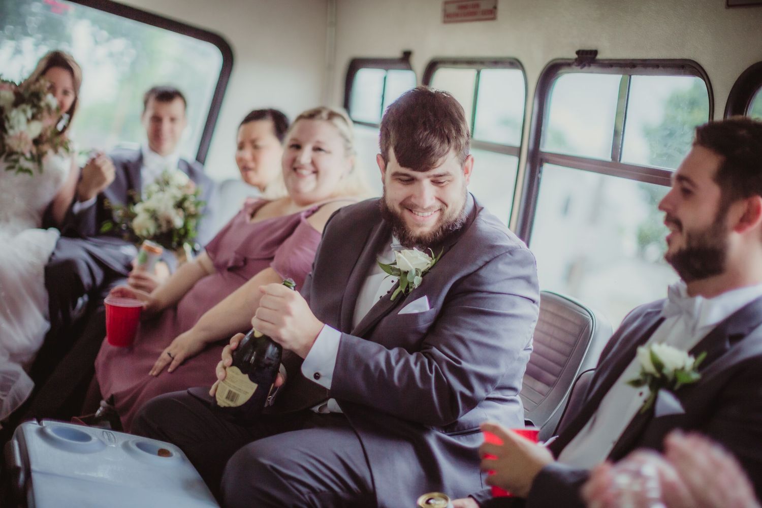 Formally dressed guests share drinks and laughter during transportation to wedding venue.