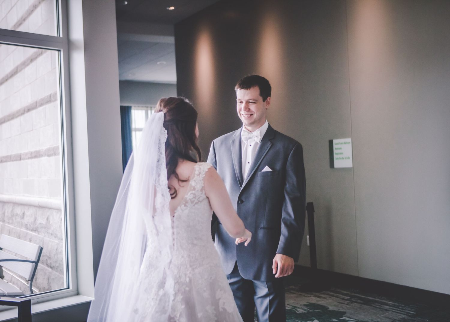 Newlyweds share a tender moment by a window in their wedding attire.