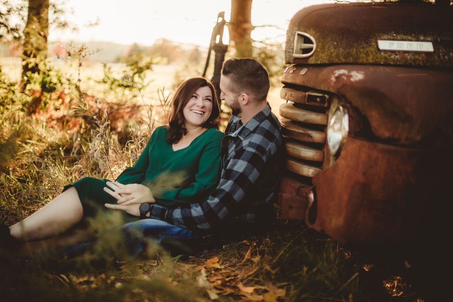 Couple shares intimate moment while sitting beside vintage truck in autumn setting.