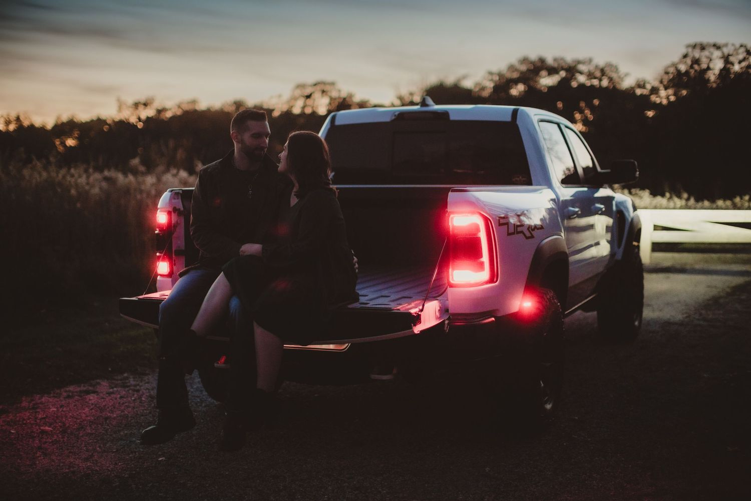Silhouetted figures on pickup truck tailgate with glowing red lights at sunset.