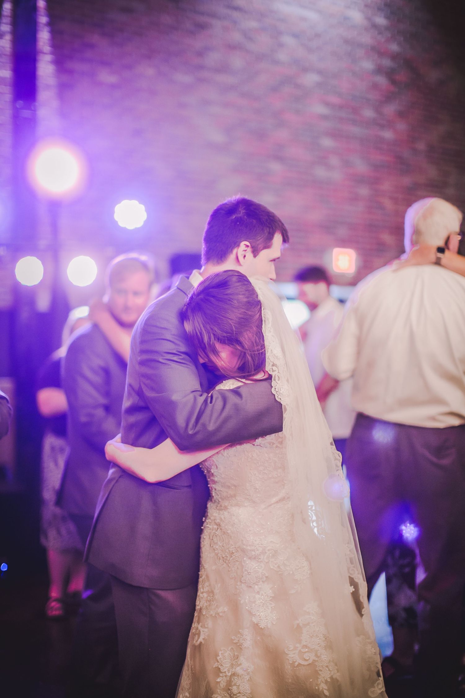 A couple shares a slow dance under purple lighting at their wedding reception.