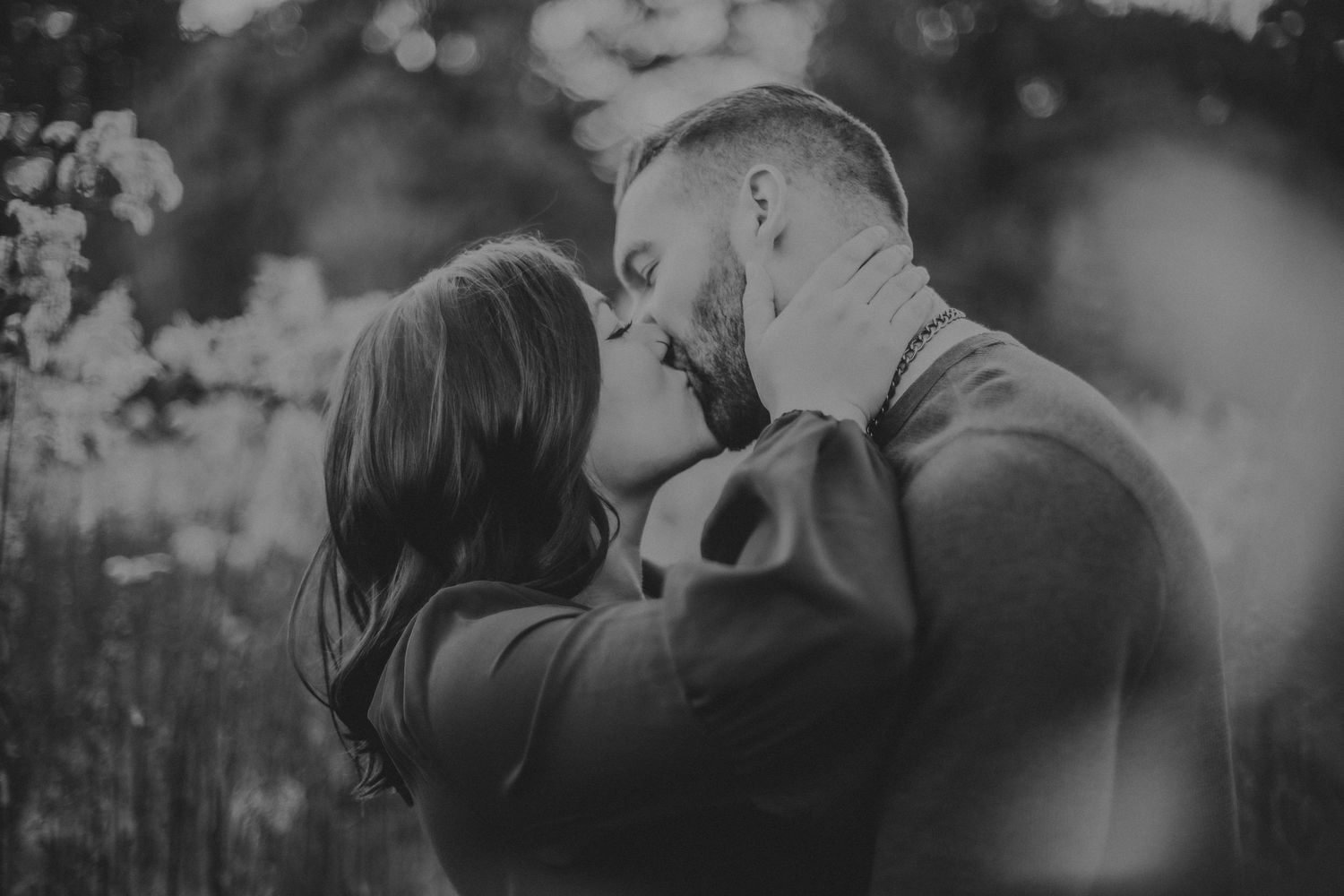 Black and white photo of intimate kiss between couple in natural setting.