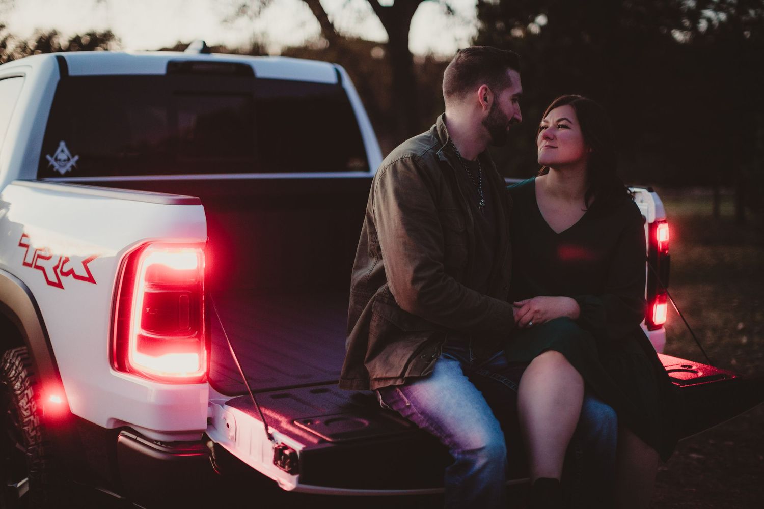 Romantic couple sitting on pickup truck tailgate at sunset with glowing red taillights.
