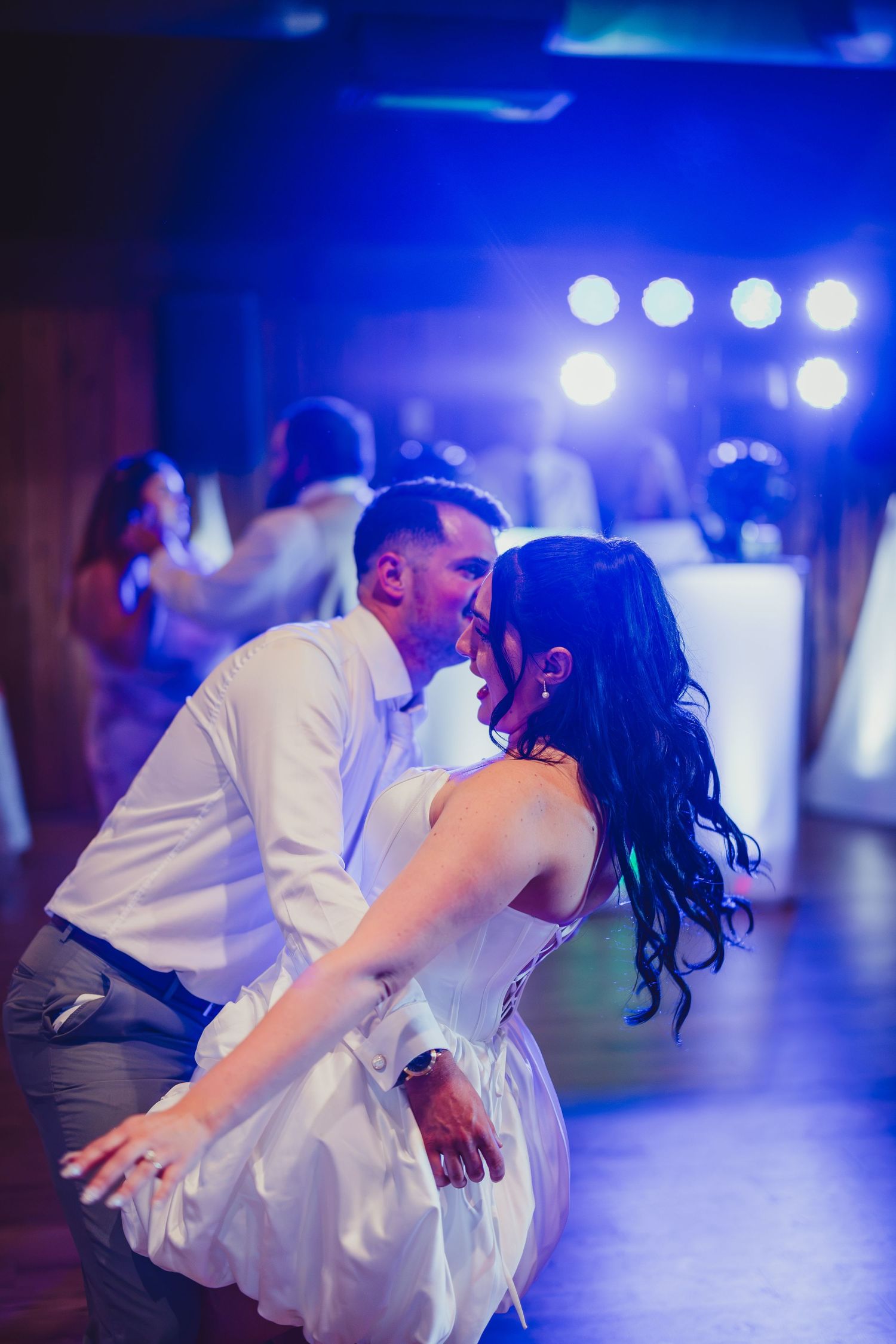 Bride and groom share a romantic first dance kiss under blue stage lights at their wedding reception.