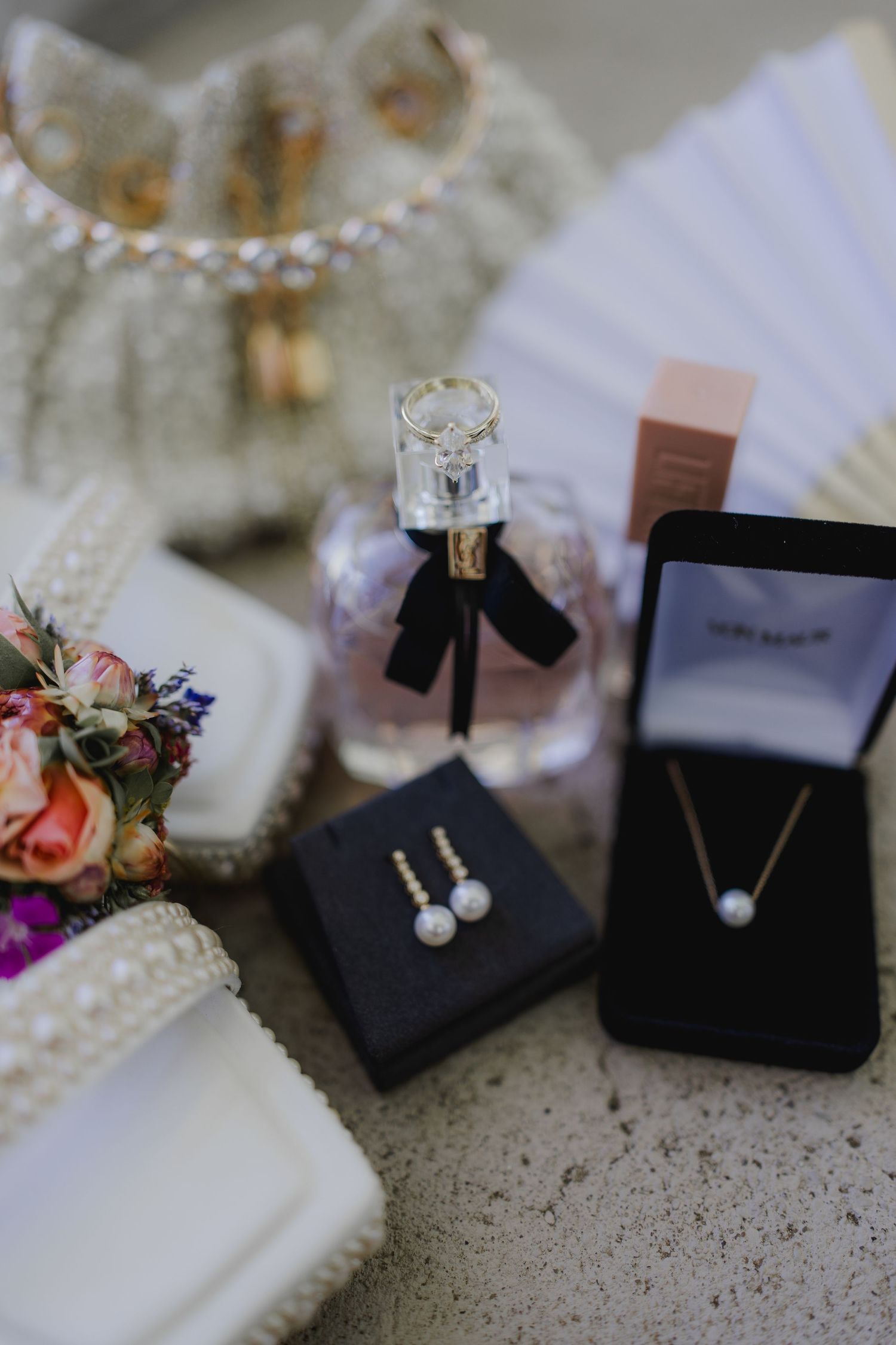 Elegant bridal accessories featuring pearl jewelry set, perfume bottle, and floral bouquet.