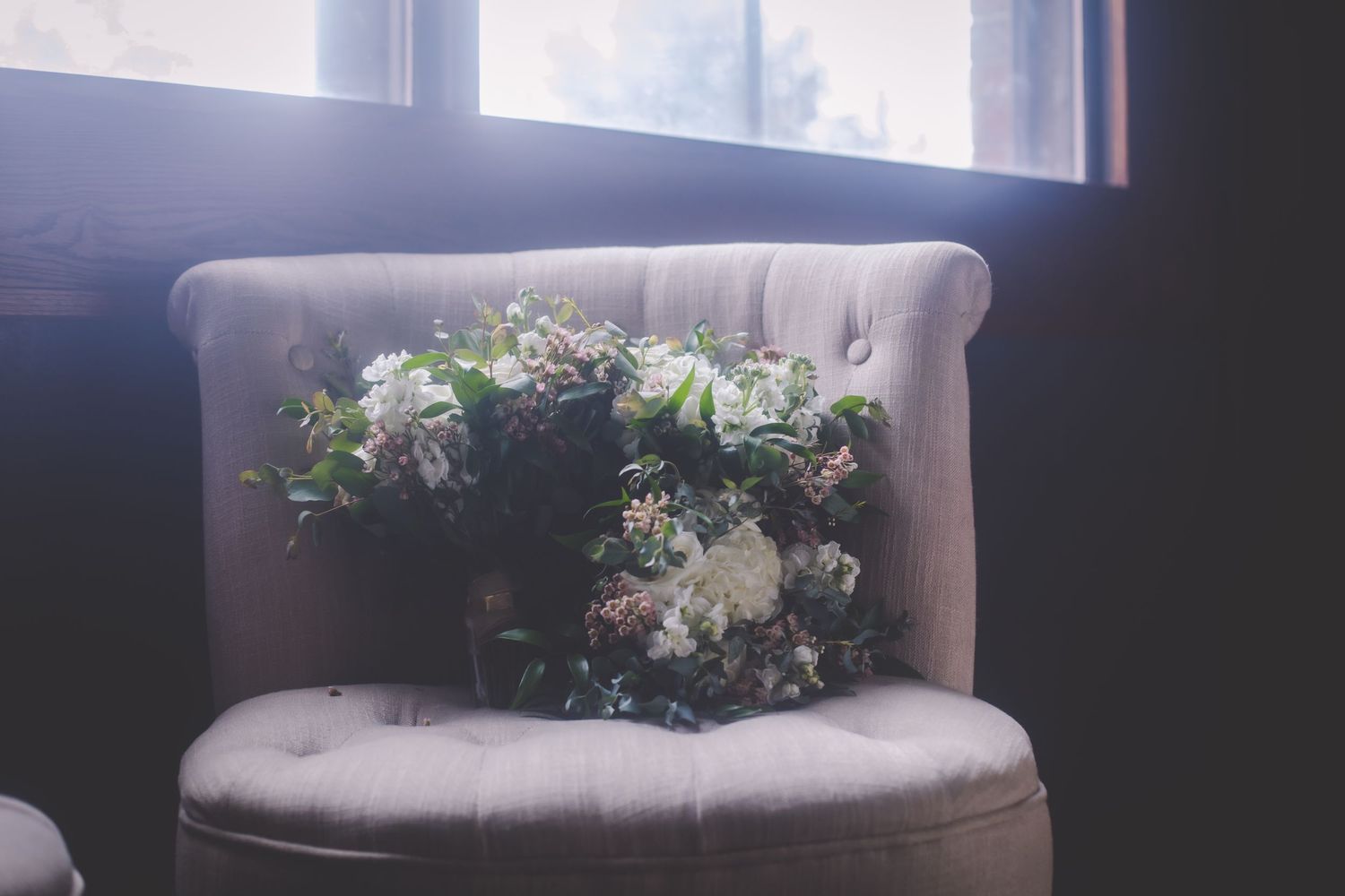 Gray upholstered chair decorated with fresh flower arrangement by window.