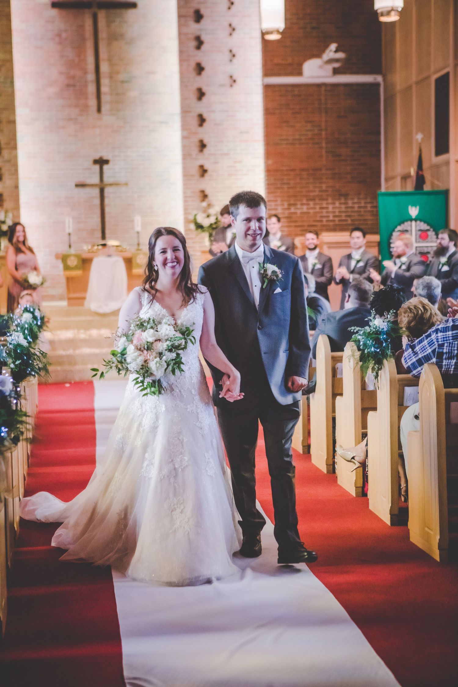 Wedding party lined up along church aisle decorated with floral arrangements.