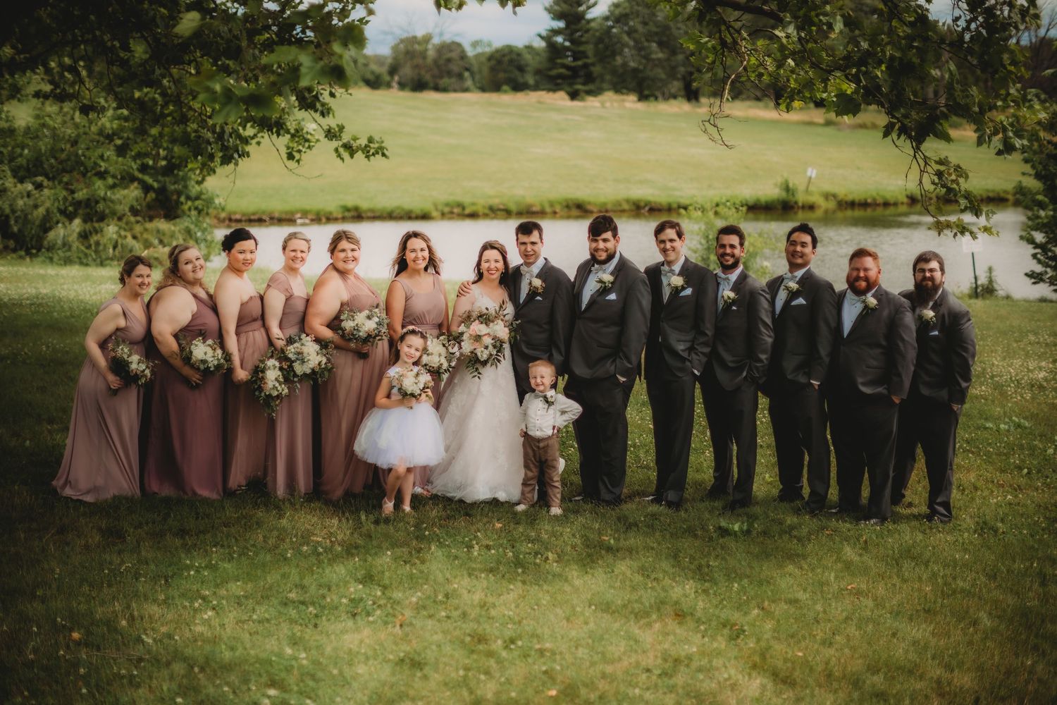 Wedding party poses outdoors with bridesmaids in mauve dresses and groomsmen in dark suits.
