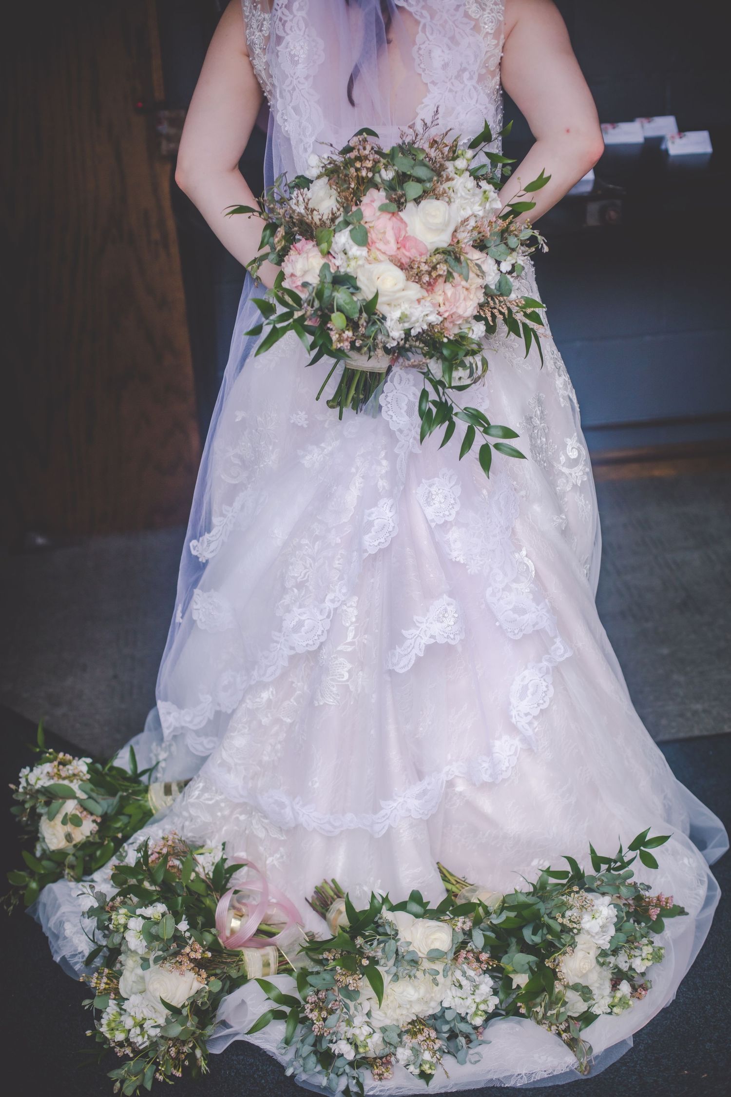 Bride holding pink and white bouquet with lace dress details visible.