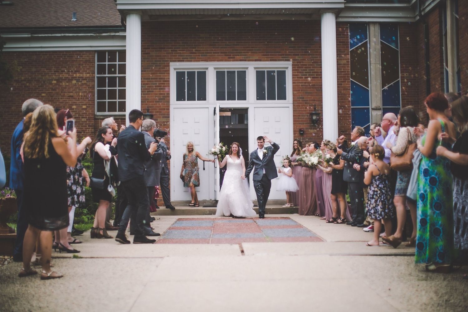 A crowd of wedding guests lined up outside a brick church building with white columns.