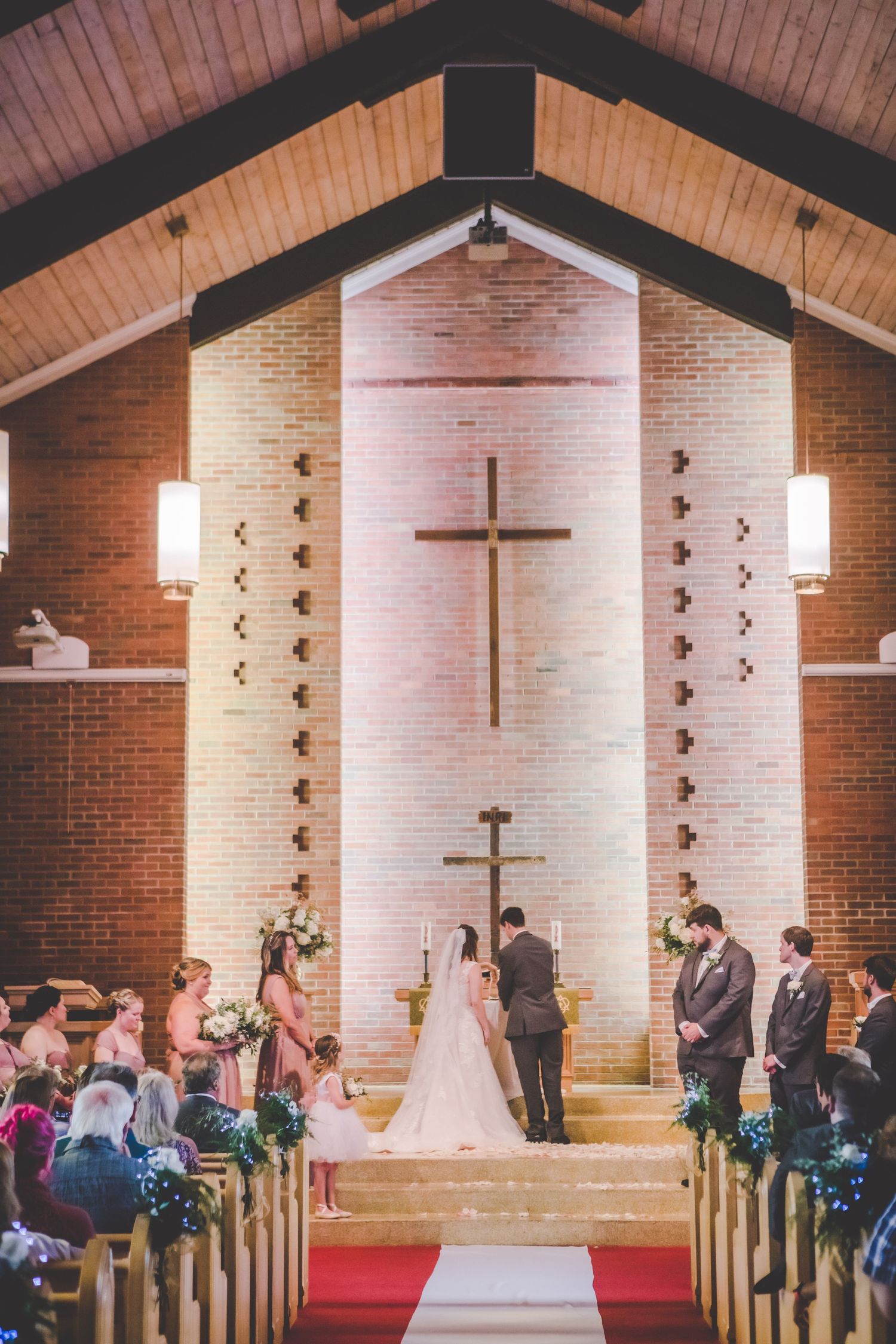 Traditional church wedding ceremony with exposed wooden beams and brick walls featuring prominent cross.