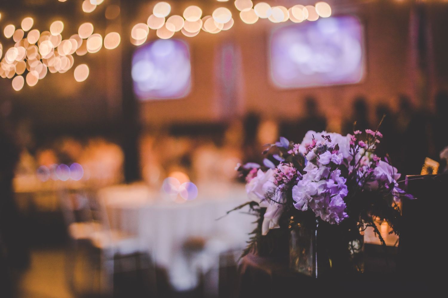 Purple floral centerpiece at wedding reception with bokeh lights in background.