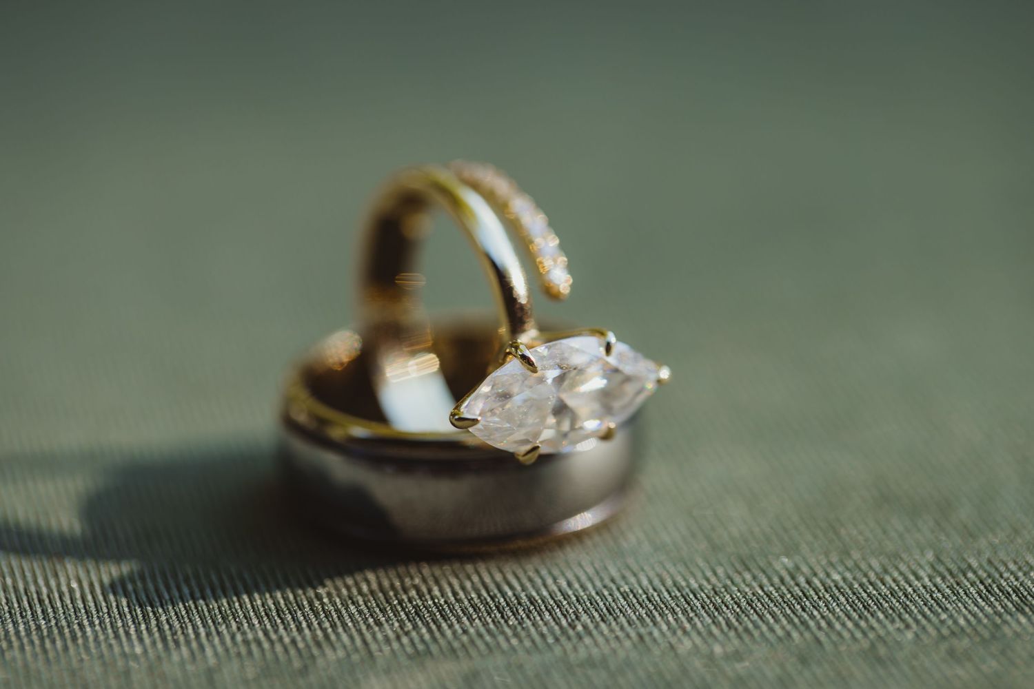 Close-up of a diamond marquise engagement ring and gold wedding band resting on a soft green surface.