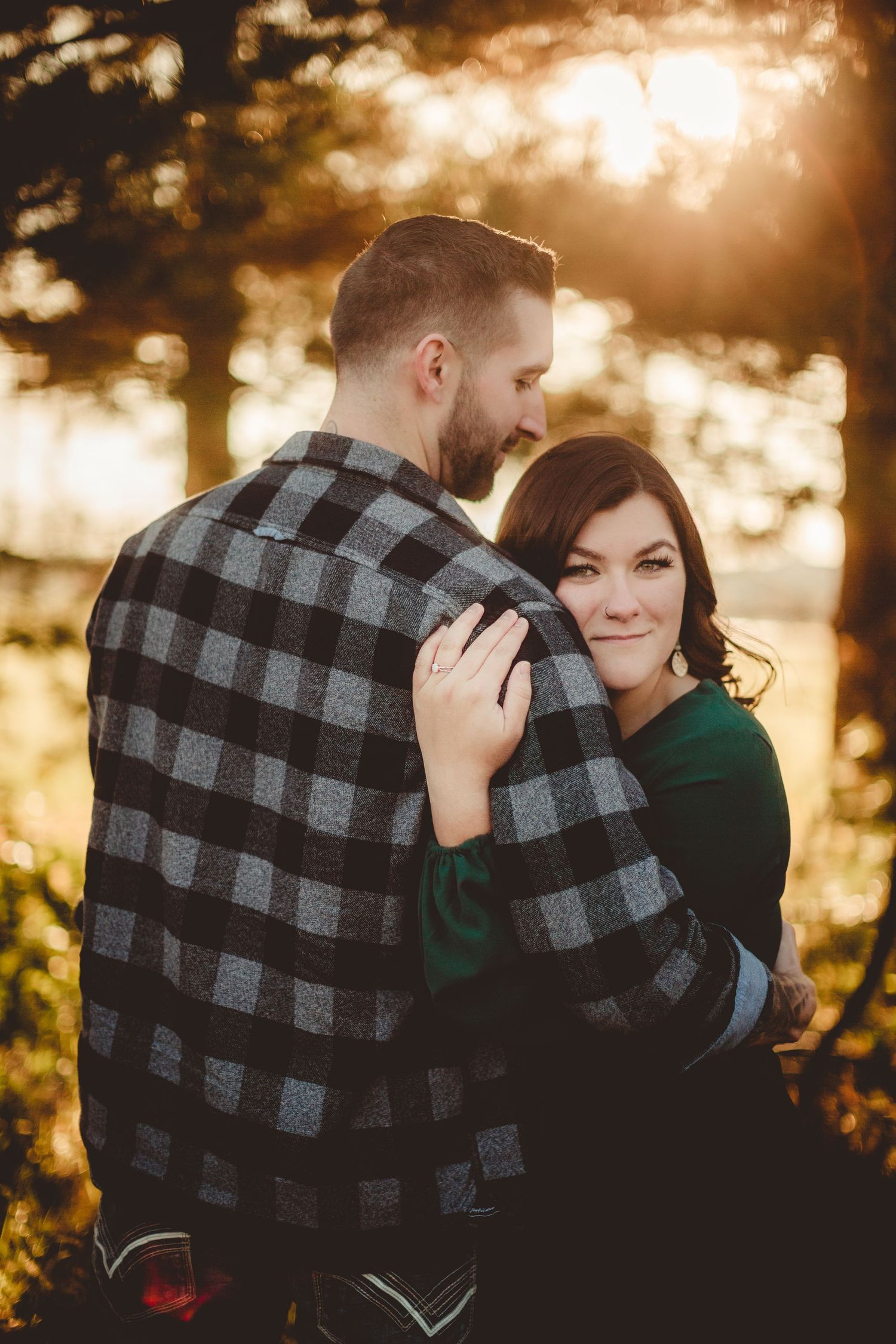 Couple embracing in front of golden sunset wearing plaid shirt and green dress.