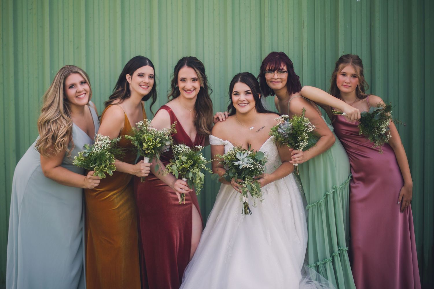 Bridal group wearing mix of dusty rose and blue dresses poses together outdoors.