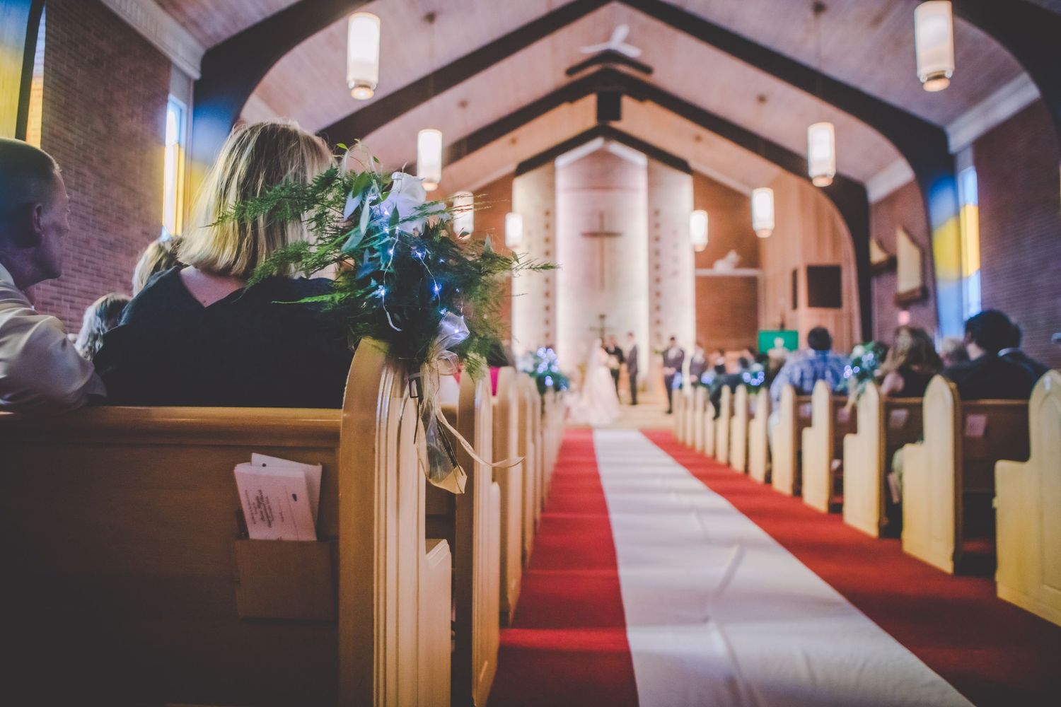 Church sanctuary with red carpet aisle and wooden pews decorated with blue floral arrangements.