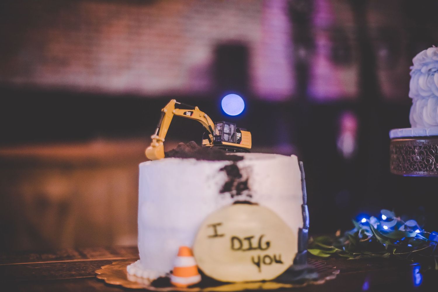 Construction themed cake decoration with miniature excavator and traffic cones on white frosting.