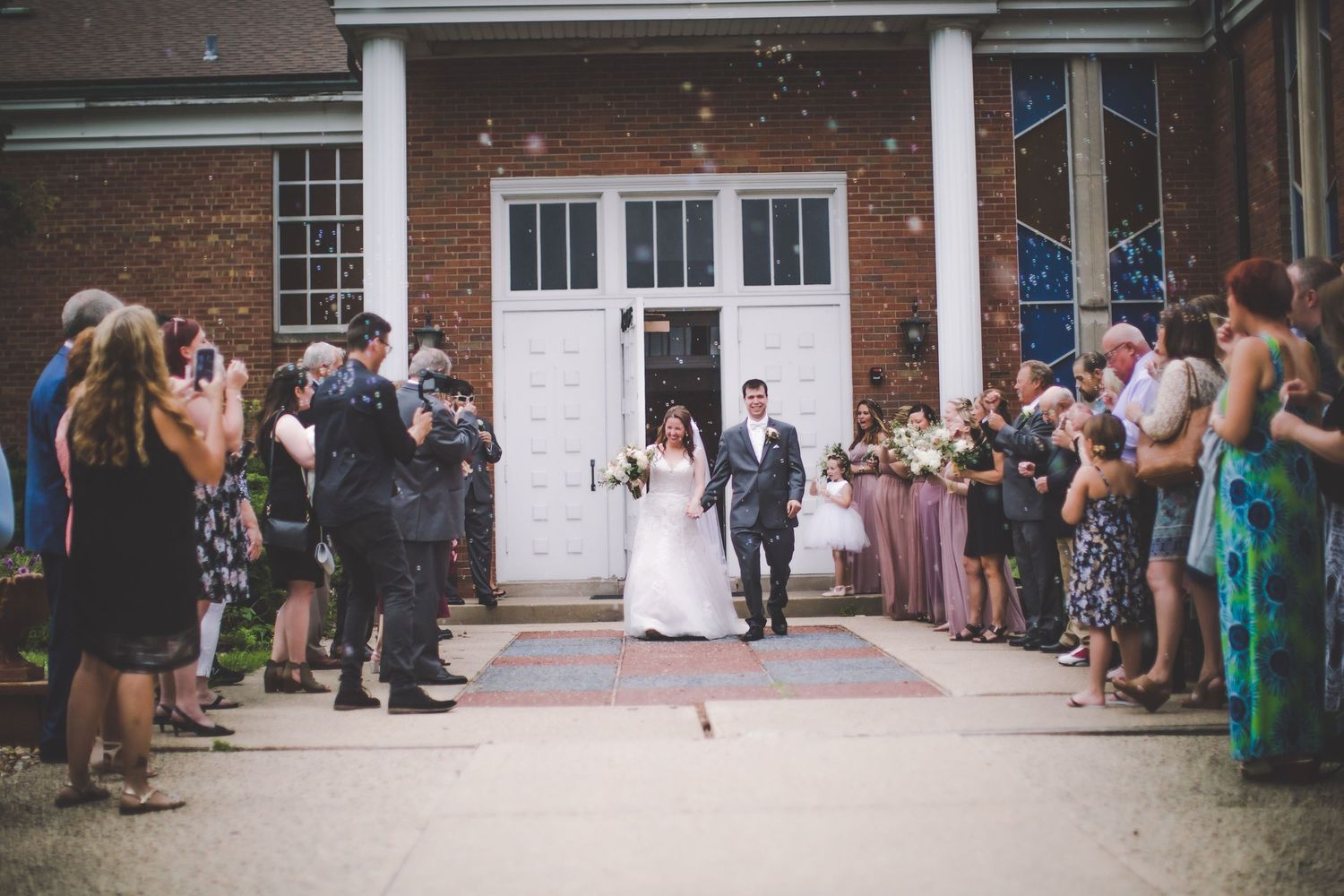 Wedding ceremony attendees stand in rows along a brick building entrance.