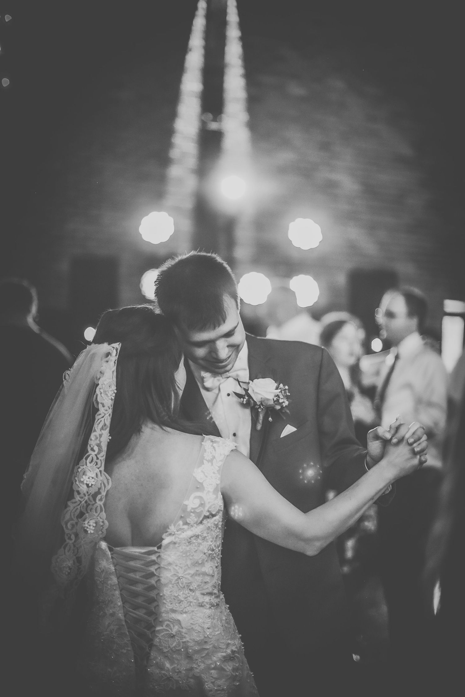 Black and white photo captures dancing couple at wedding reception with soft backlighting.