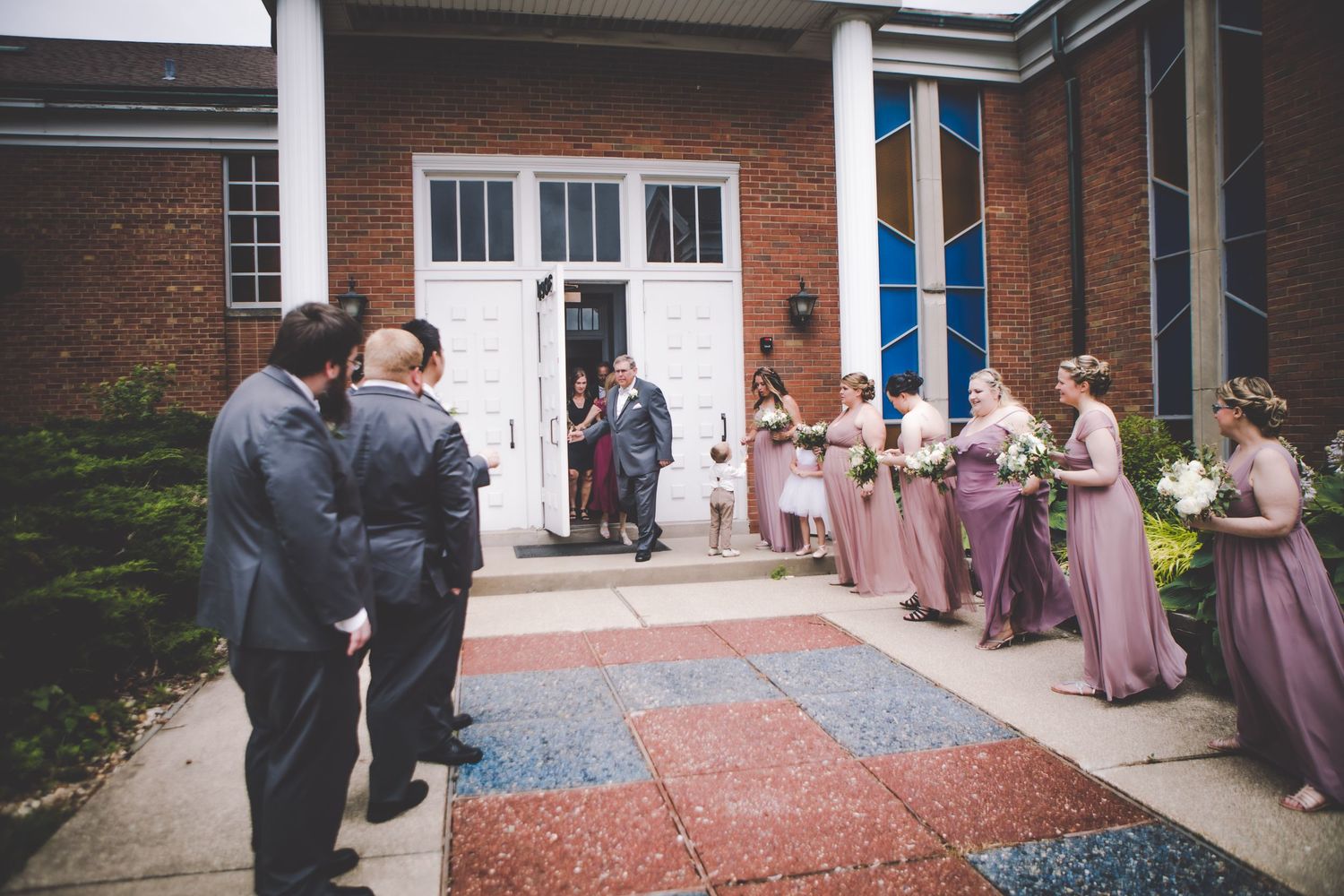 Wedding party gathering outside brick building with white columns.