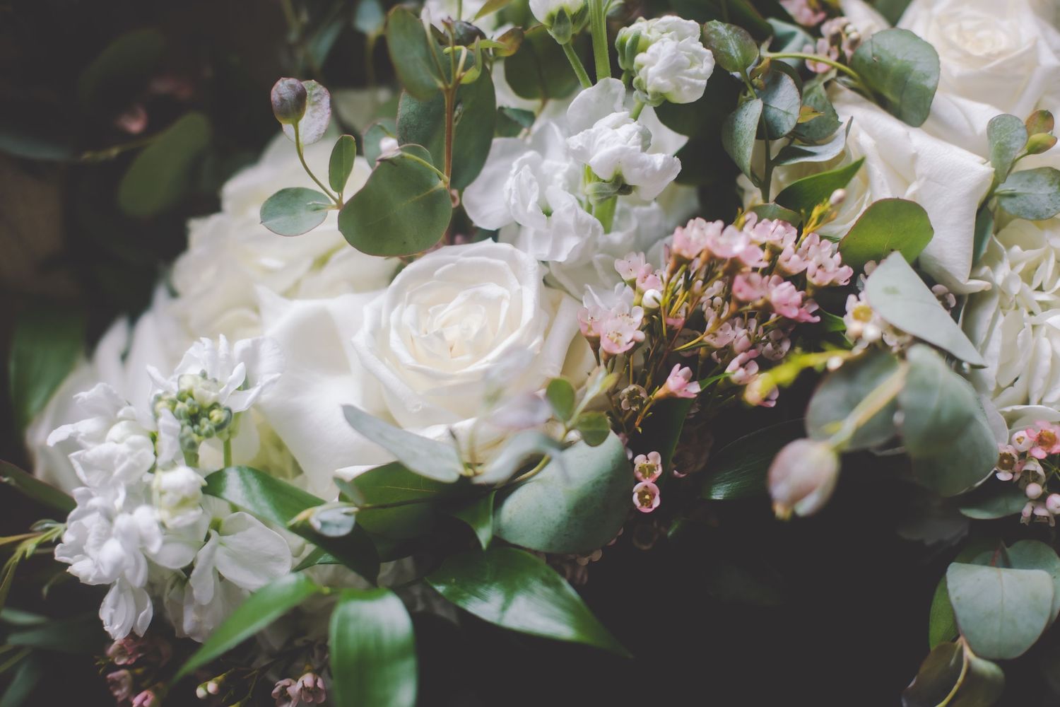 White roses and delicate pink flowers arranged in an elegant wedding bouquet with greenery accents.