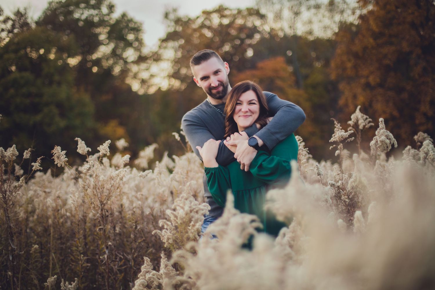 Couple laughing together in rustic autumn field with golden dried grasses.