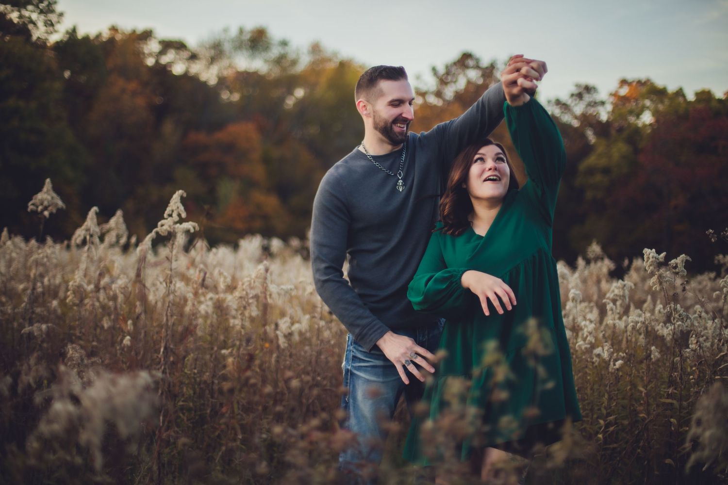 Candid couple photography in a rustic field with autumn colors in the background.