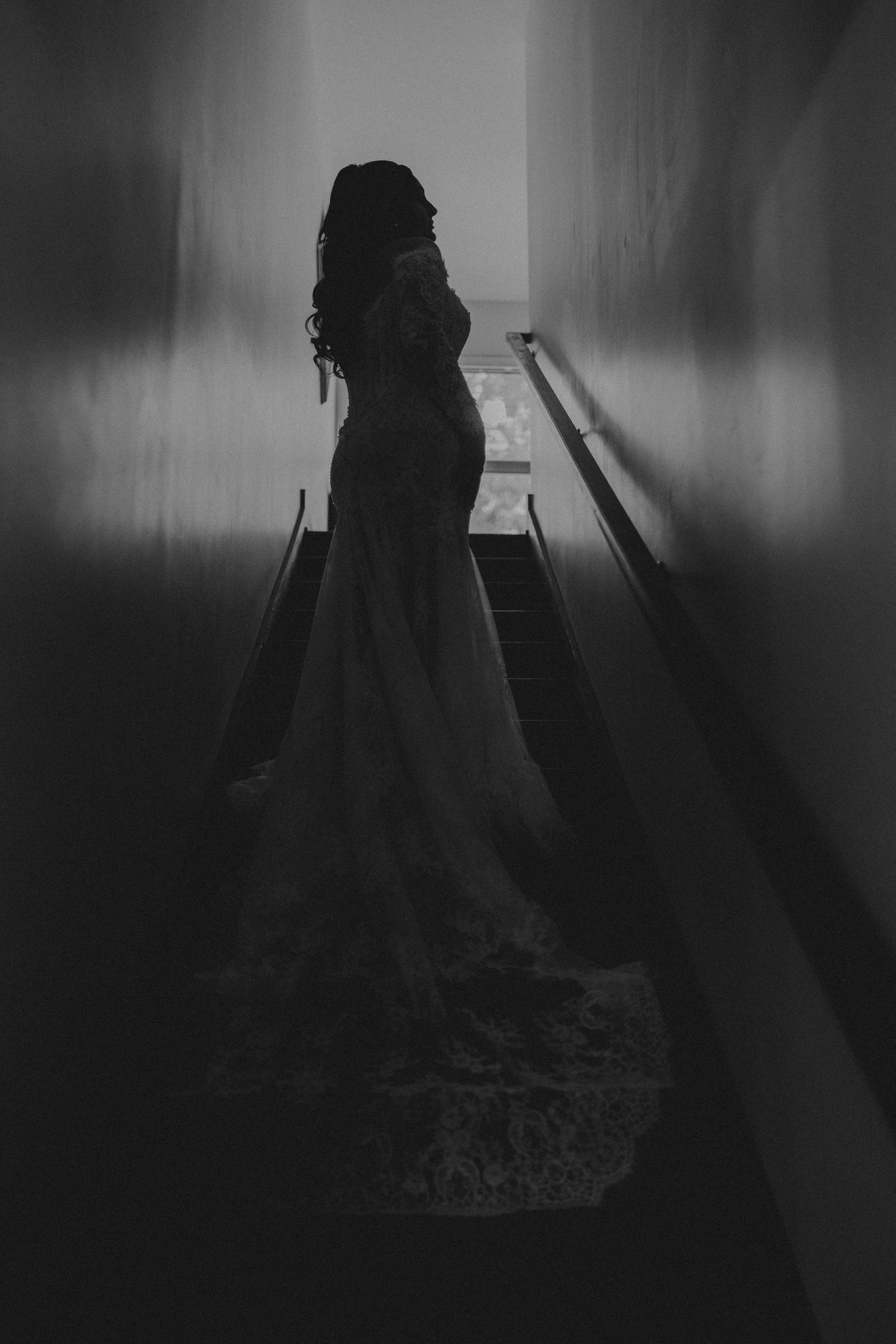 Silhouette of a bride in a flowing wedding gown standing on stairs in a dramatic black and white photo.