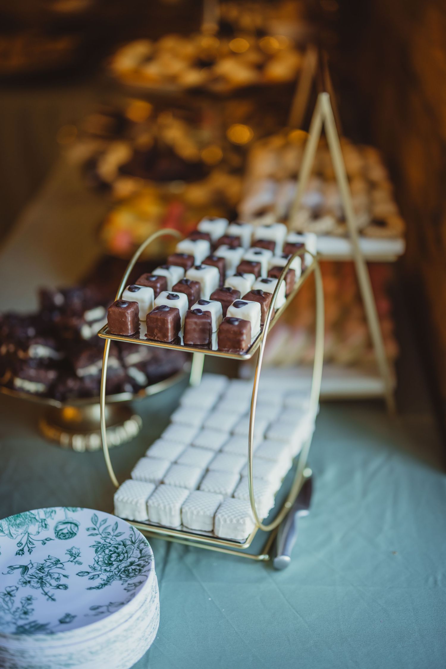 Gold tiered dessert display stand with chocolate and white petit fours at an elegant wedding dessert table.