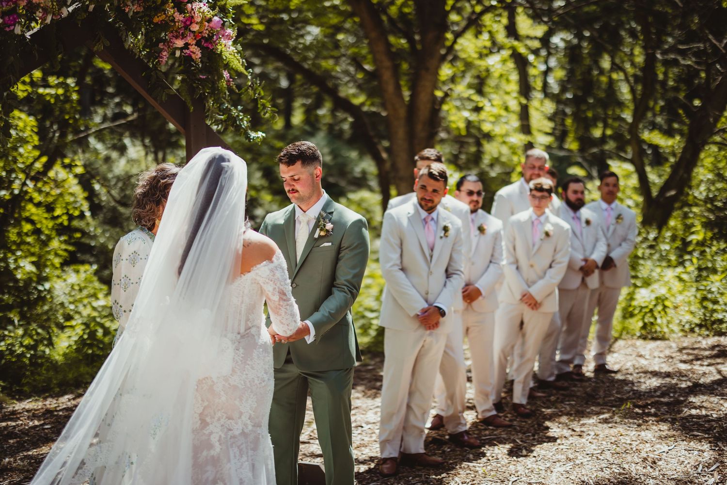 Groom reacts emotionally as bride walks down the aisle at outdoor wedding ceremony with groomsmen lined up.