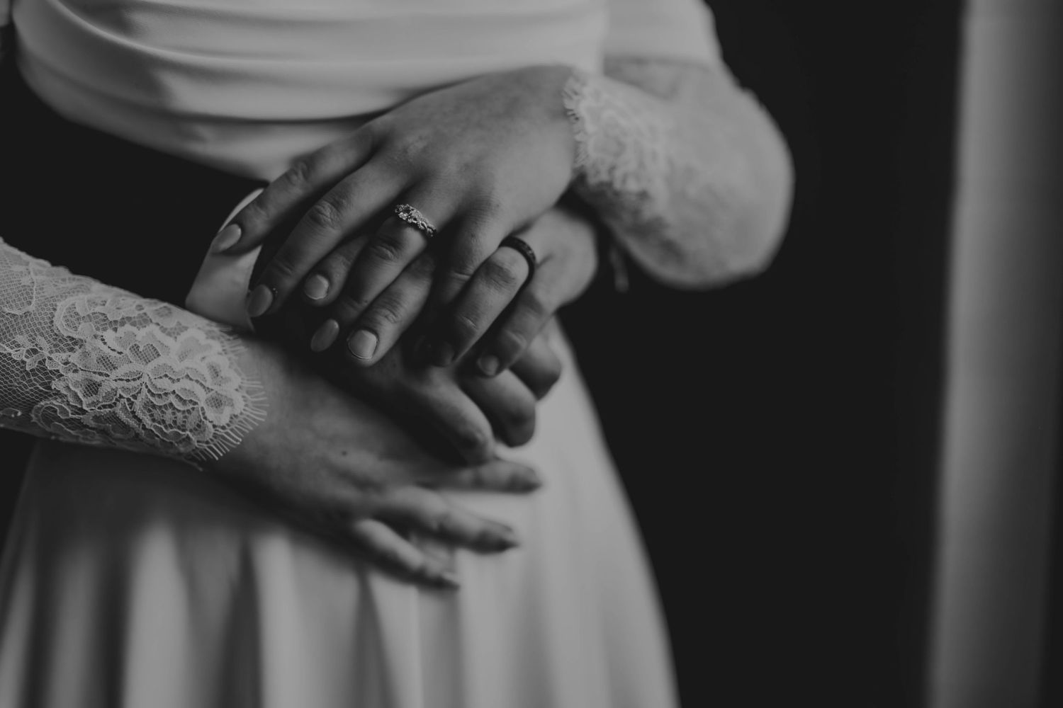 A close-up view of hands wearing wedding rings in black and white photography.