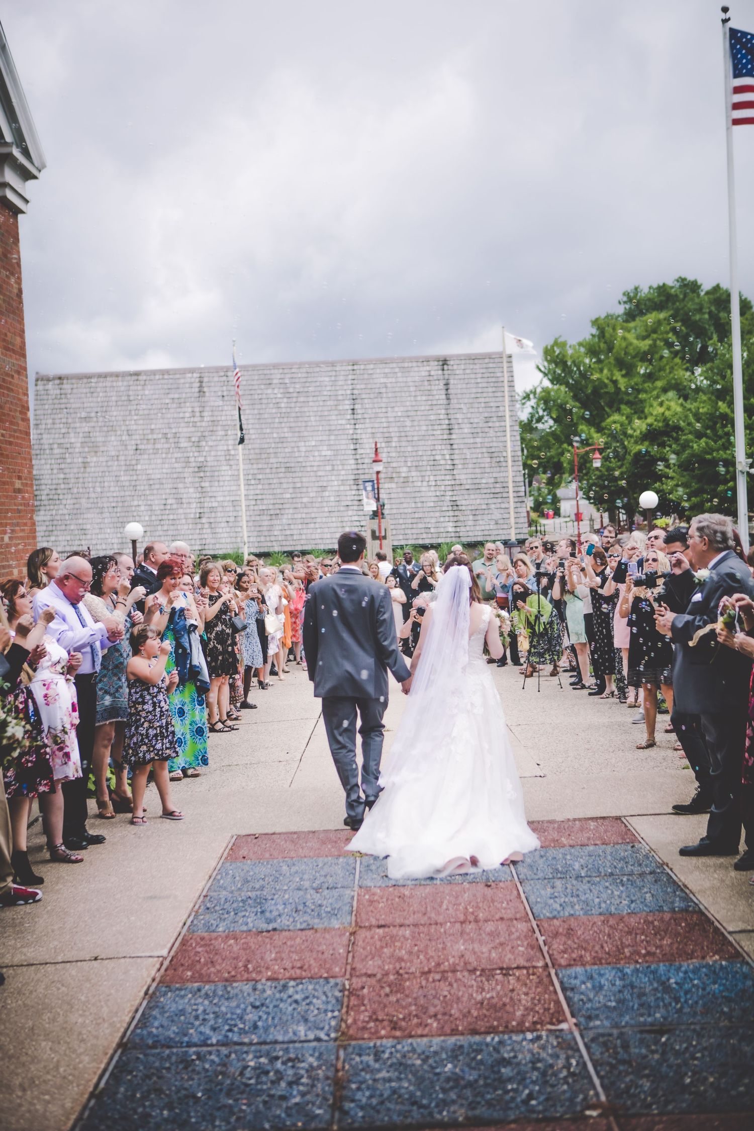 Wedding ceremony taking place outdoors with crowd gathered beside stone wall and decorative carpets.