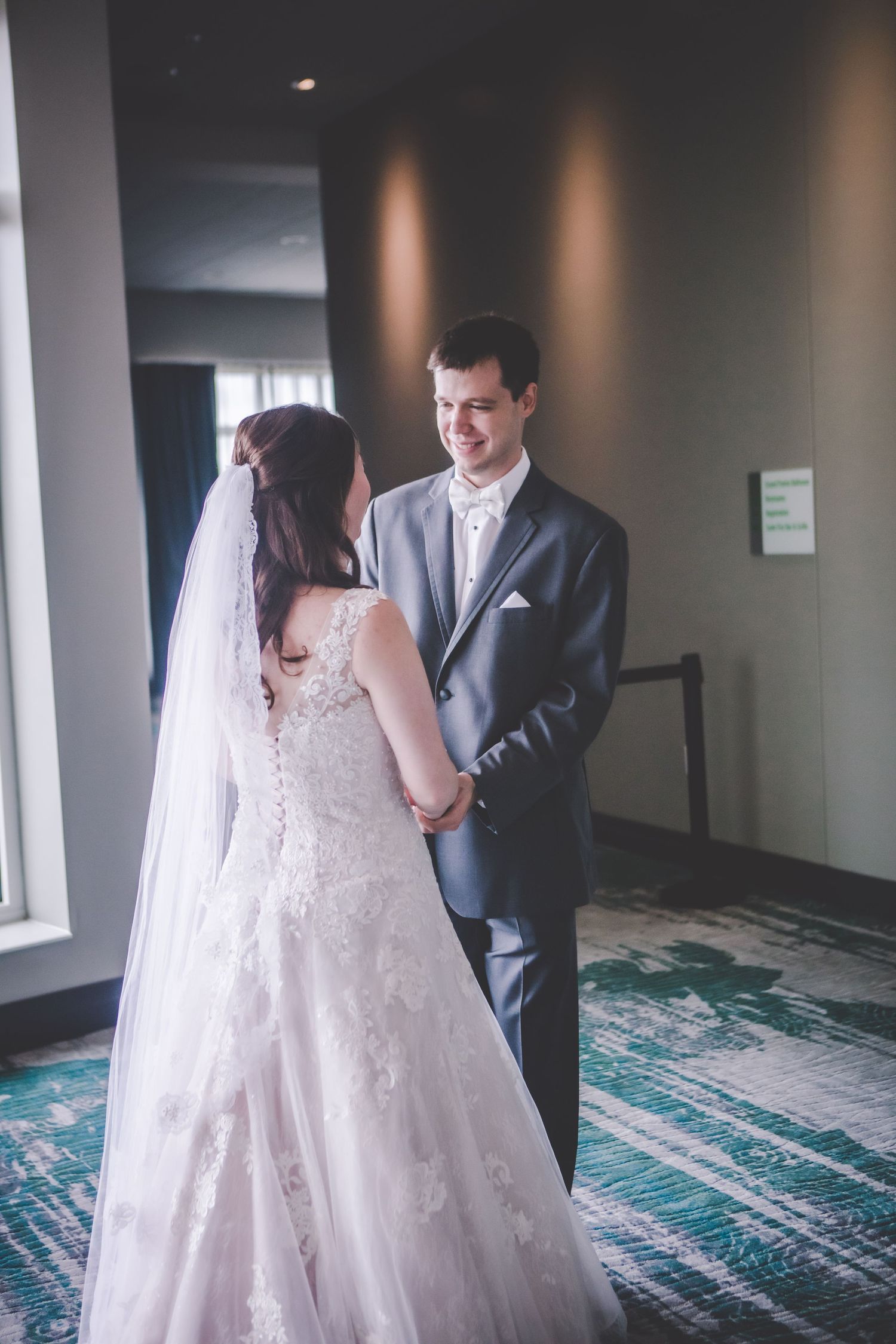 A beautiful wedding moment captured as the couple interacts by large windows.
