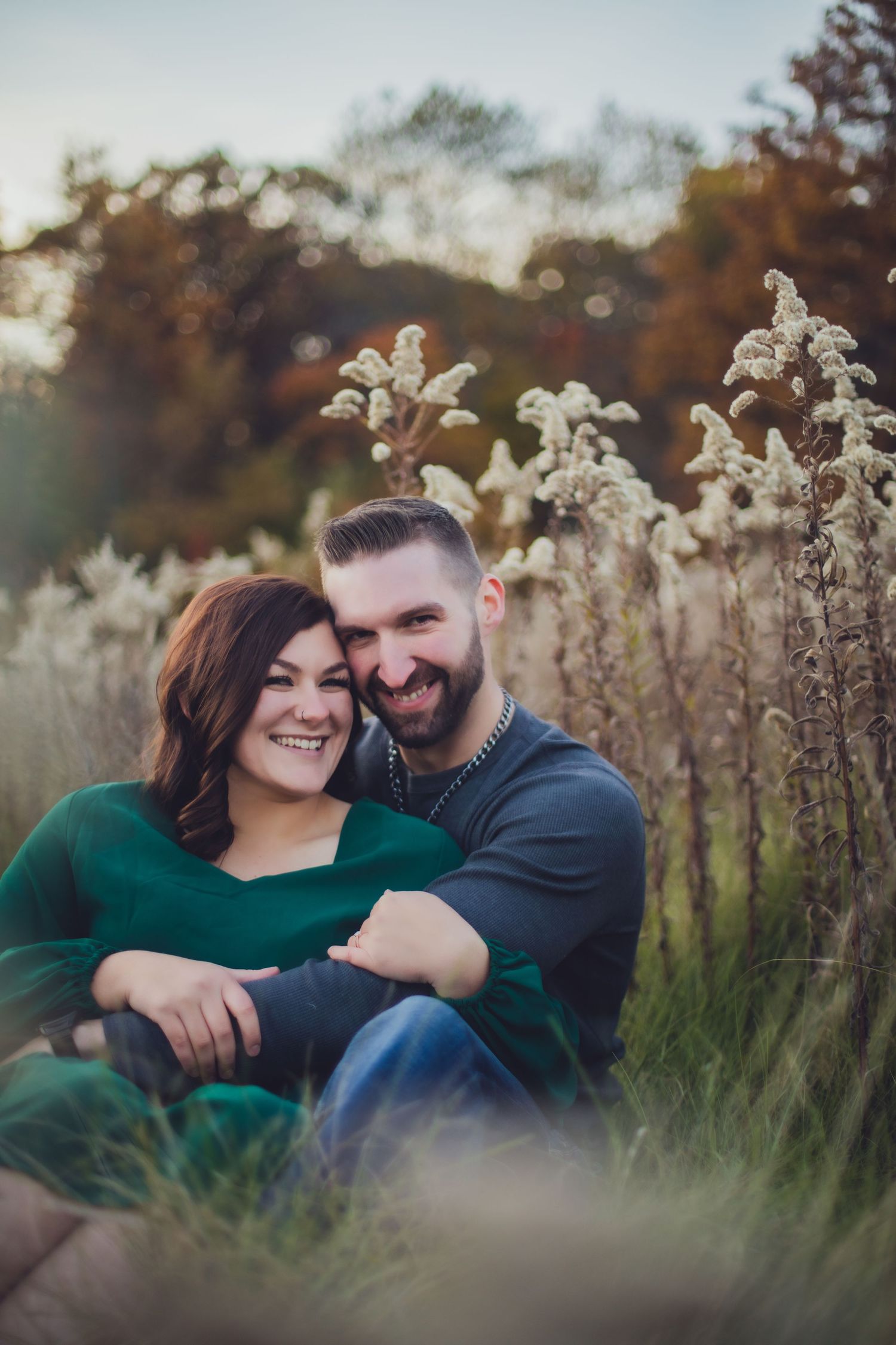 Happy couple sharing intimate moment while sitting in autumn field with dried flowers.