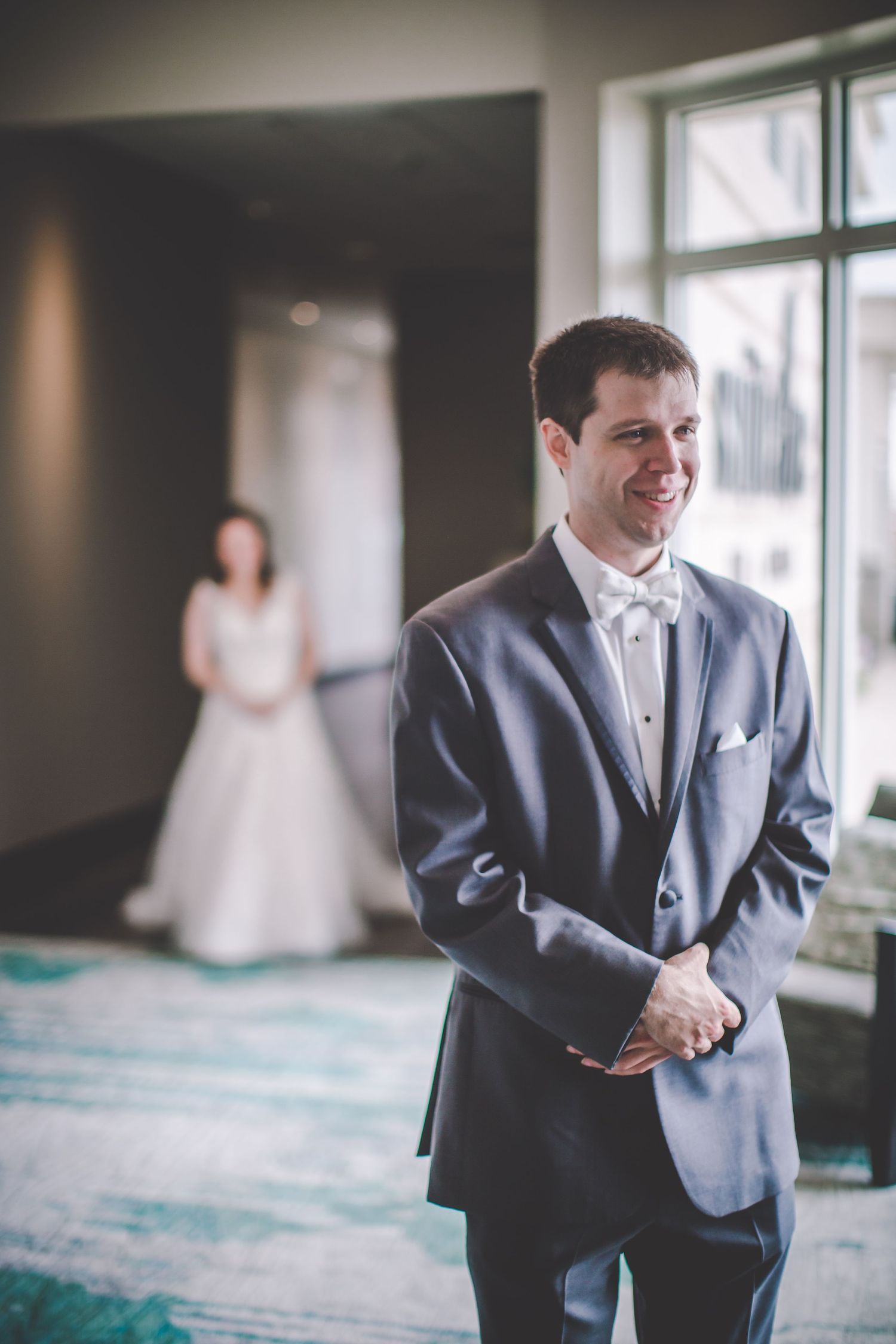 Candid wedding moment captured in natural light with white gown visible in background.