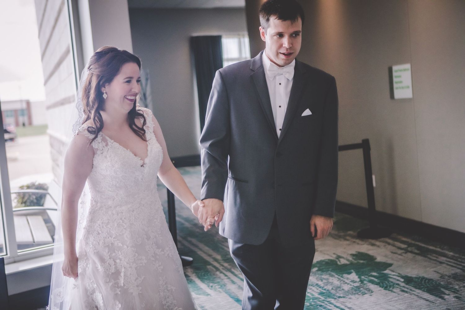 Happy newlyweds walking together on turquoise patterned carpet in a modern venue.