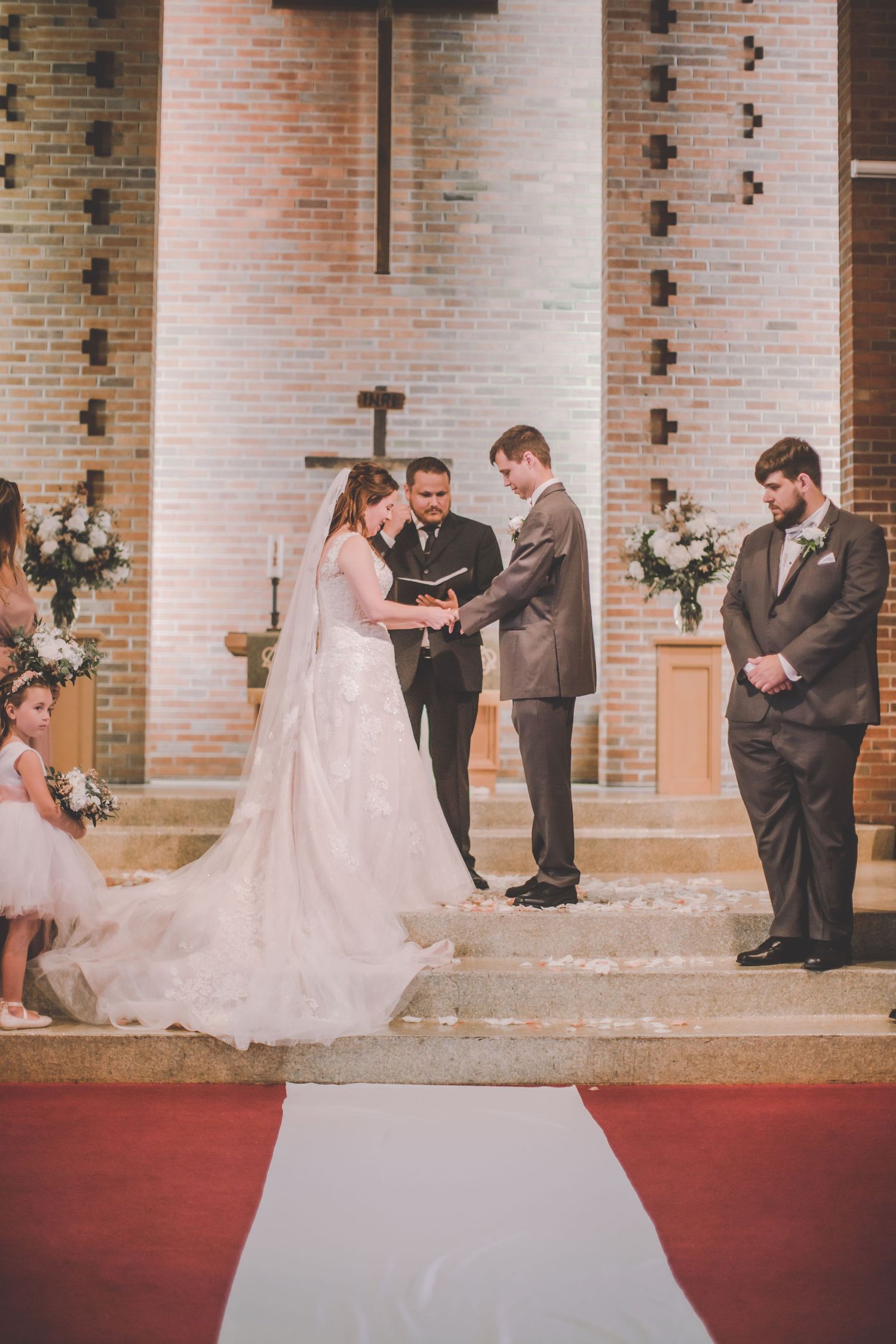 Wedding ceremony against brick columns with red carpet and formal attire.