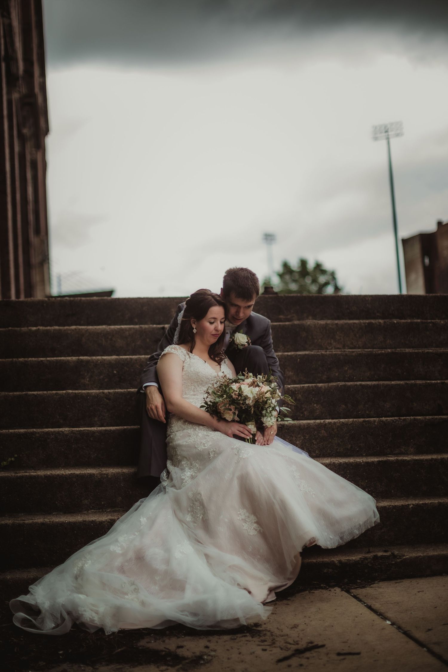 Moody wedding portrait of a couple sharing a tender moment on concrete steps.
