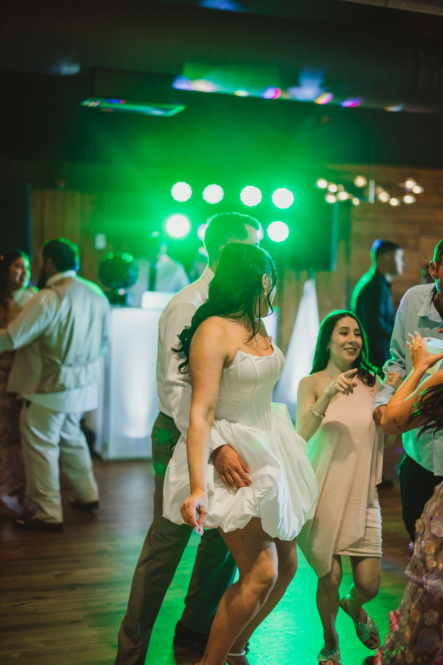 Bride and groom dancing energetically on illuminated dance floor with green stage lights at wedding reception.