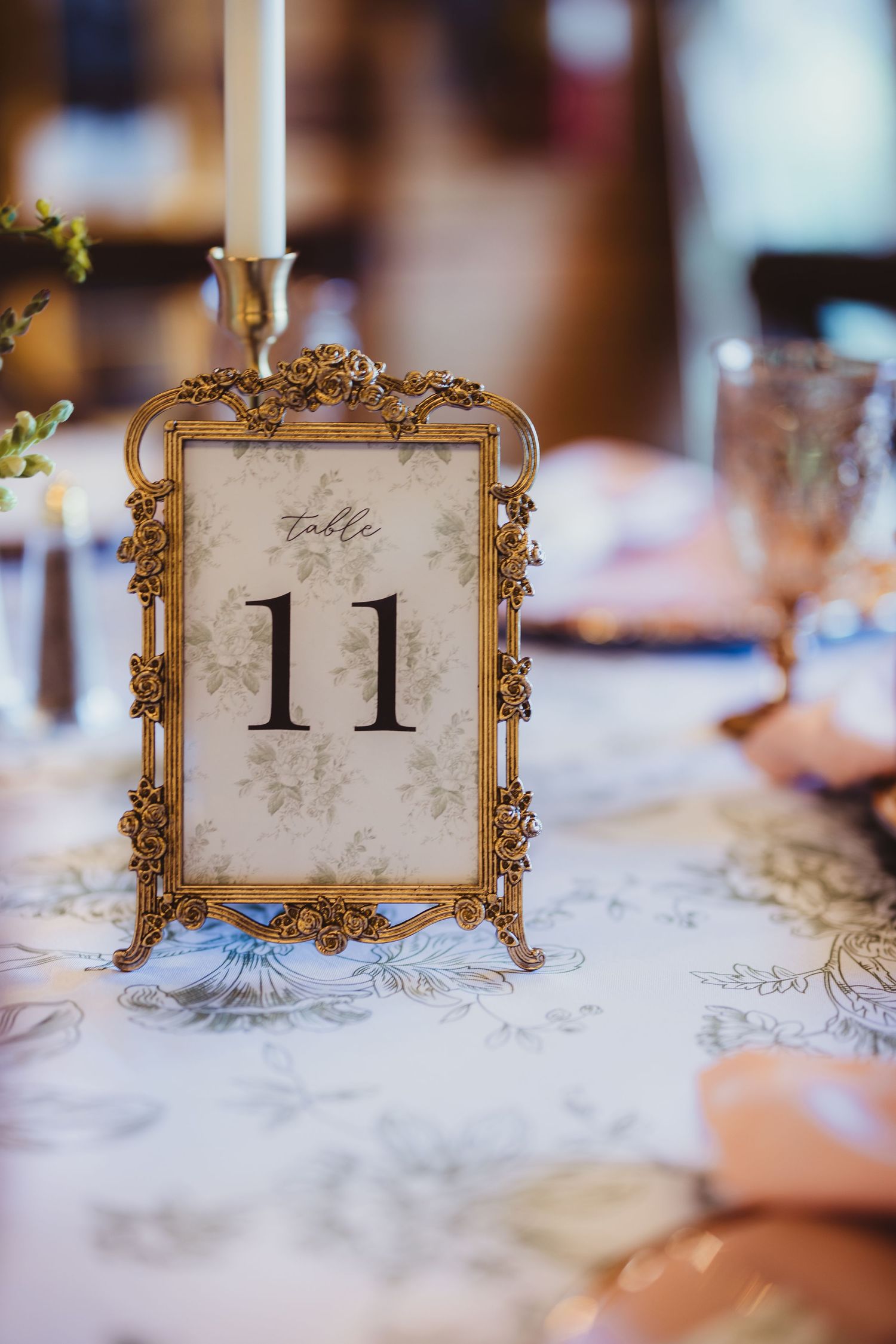 Ornate gold vintage frame displaying table number 11 on floral tablecloth at elegant wedding reception.
