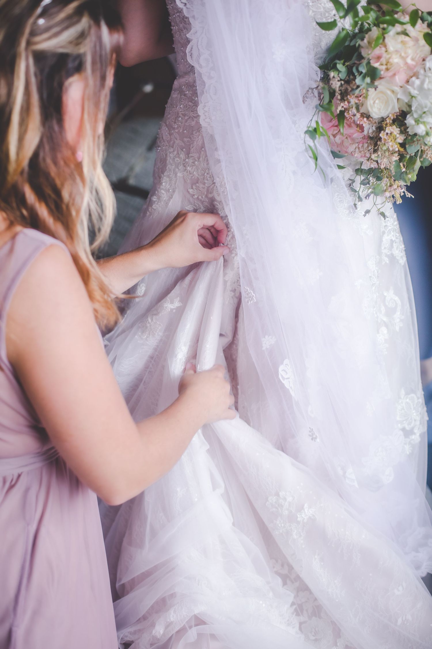 Close-up of hands adjusting intricate lace details on a white wedding gown.